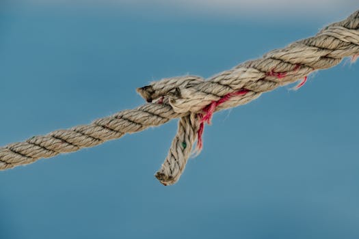 A detailed close-up photograph of a frayed nautical jute rope against a soft blue background.