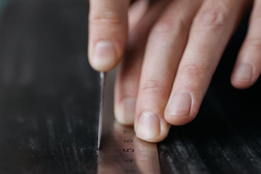 Macro shot of fingers precisely using a stainless steel ruler on a dark surface.